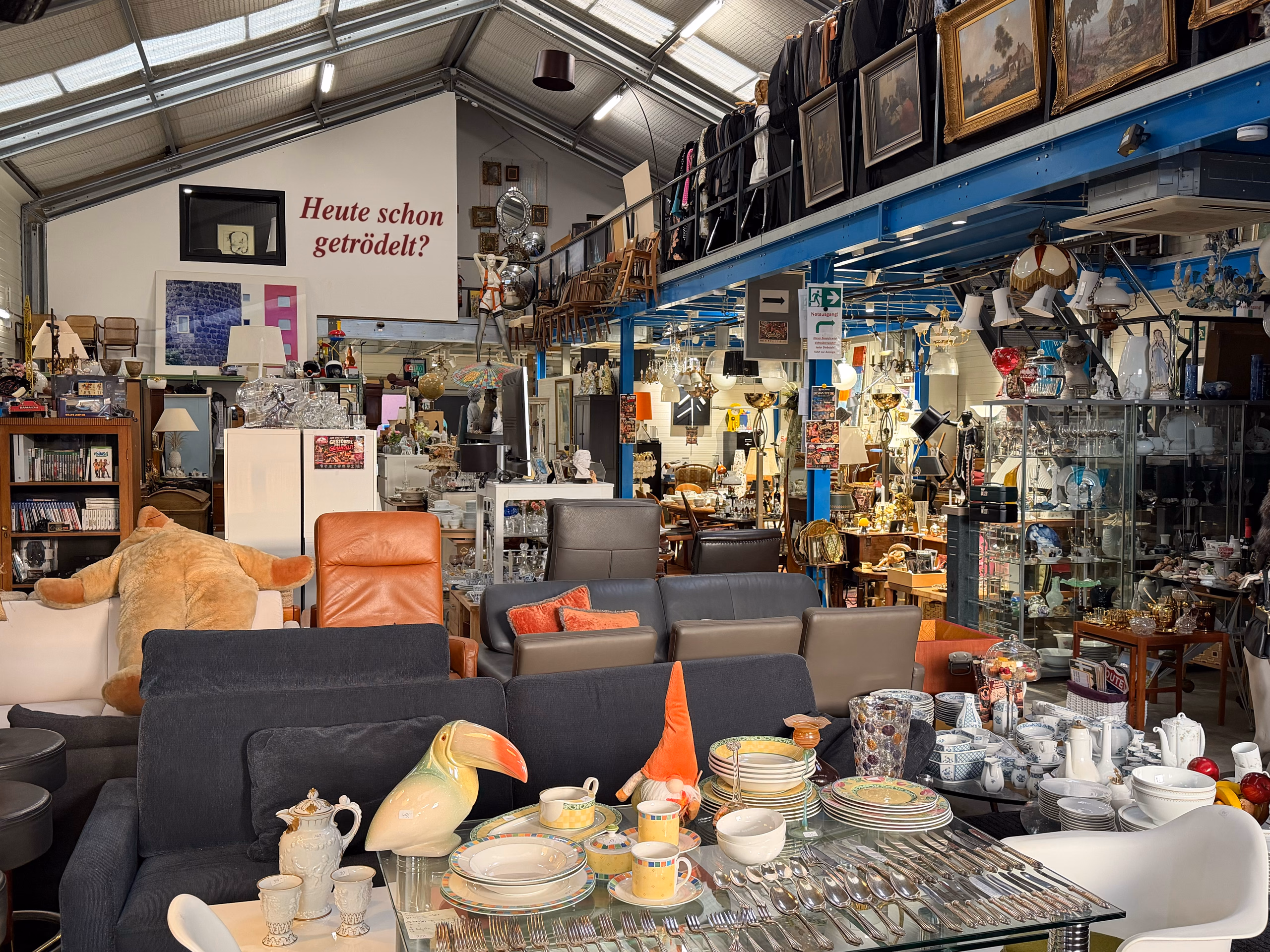 Blick in DIE HALLE mit Wandschrift „Heute schon getrödelt?“, Sofas, Porzellan und Galerie mit Ölgemälden
